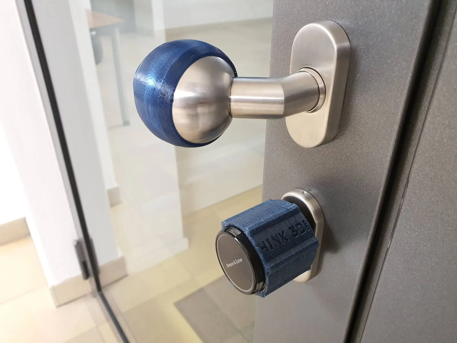 Blaue 3D-gedruckte Überzüge auf einem Türknauf und einem Schließzylinder an einer Tür