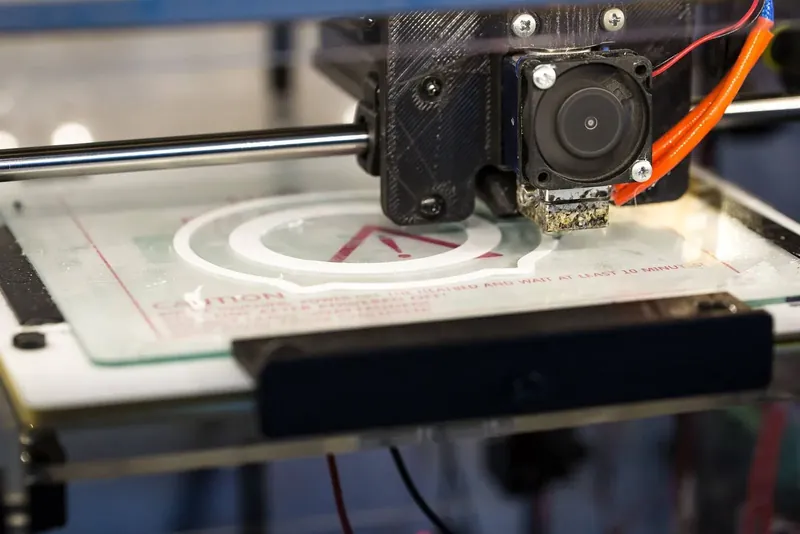 Druckkopf eines FDM-3D-Druckers über einem weißen Bauteil auf der gläsernen Druckplatte